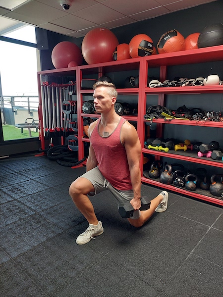 person in gym performing dumbbell lunge