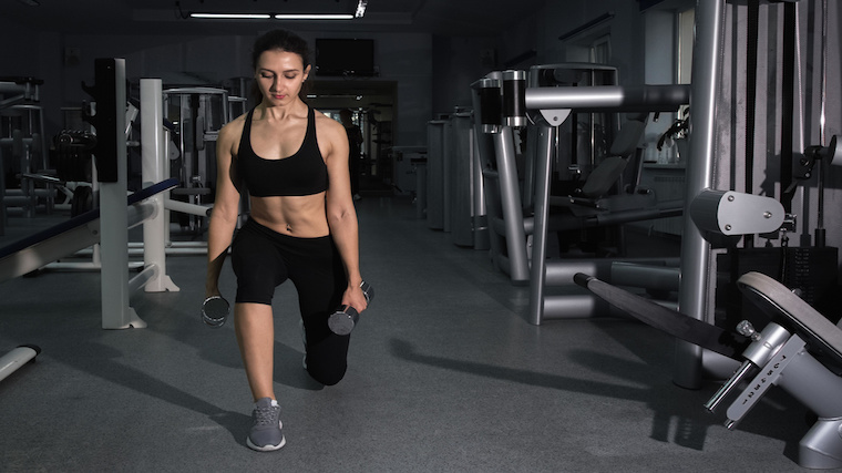 person in empty gym performing dumbbell lunge