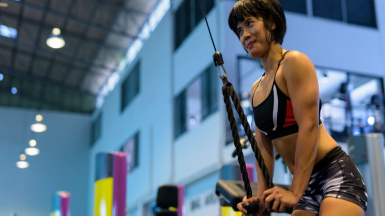 Person in gym performing triceps exercise with cables