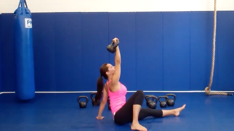 long-haired person in gym on floor lifting kettlebell