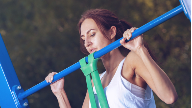 woman outdoors performing pull-up with resistance band