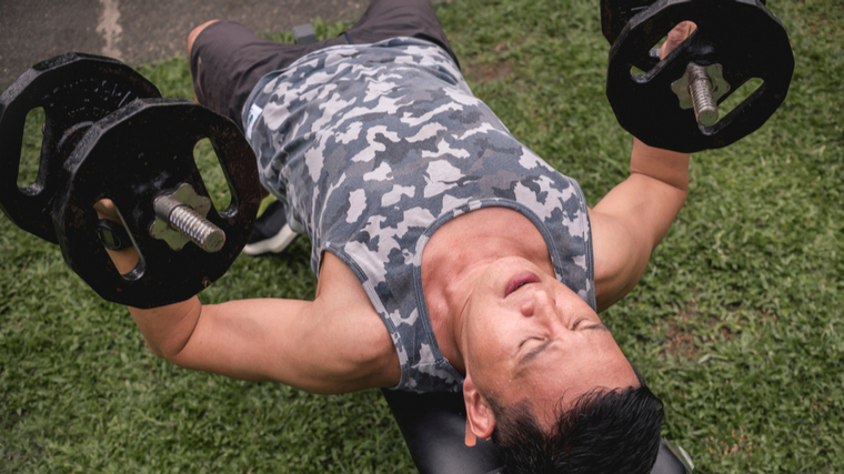 Man outdoors on flat bench lifting dumbbells