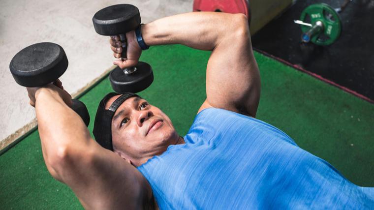 Man lying down performing triceps exercise with dumbbells