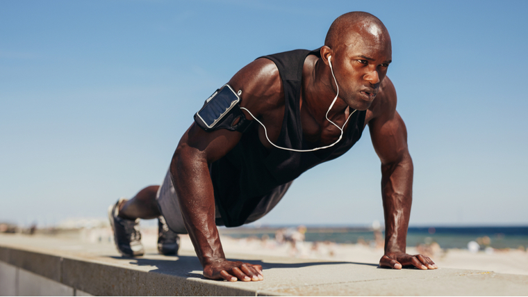 Bald man wearing headphones performing push-ups outdoors