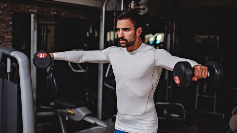 Man in gym performing lateral raise with dumbbells