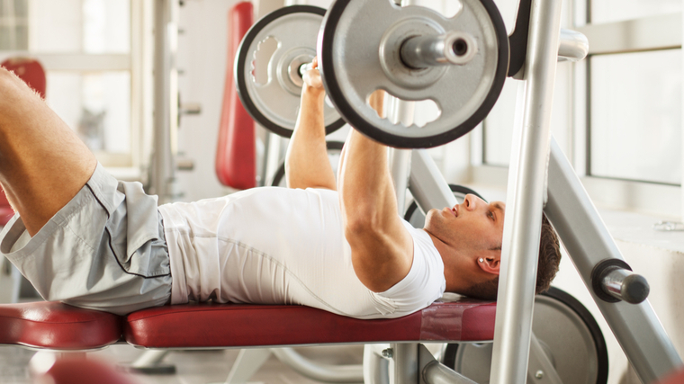 Man performing bench press exercise with legs in the air