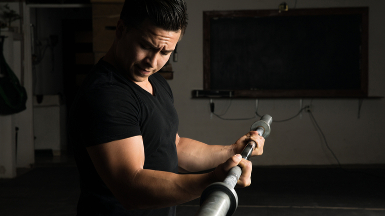 person in dark gym curling barbell